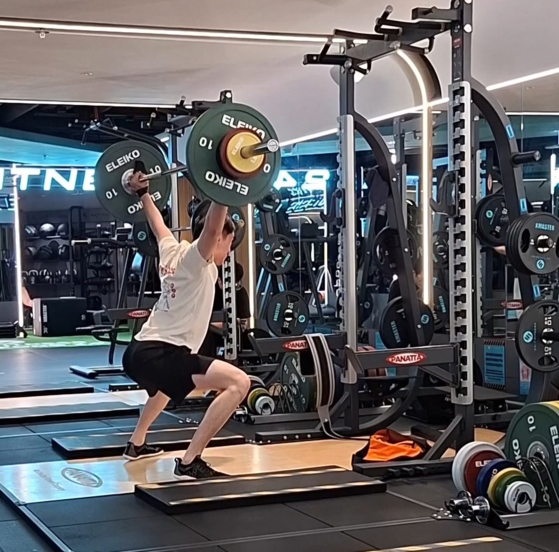 Donald Tsang performing an overhead barbell lift in a gym