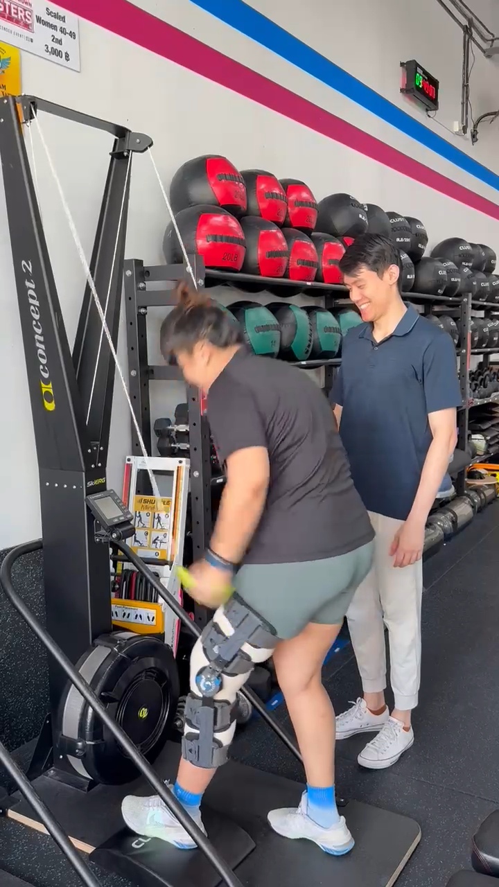 Donald coaching a patient in a knee brace using a SkiErg